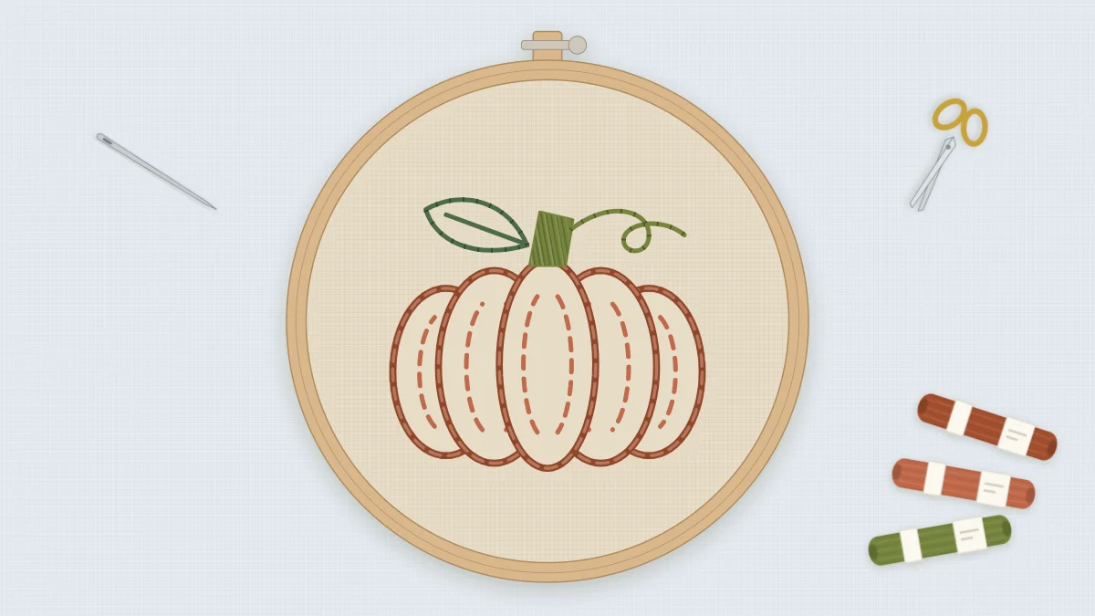 Finished embroidered pumpkin in a 5-inch hoop on natural linen in rust and terracotta with a green stalk, tendril, and leaf